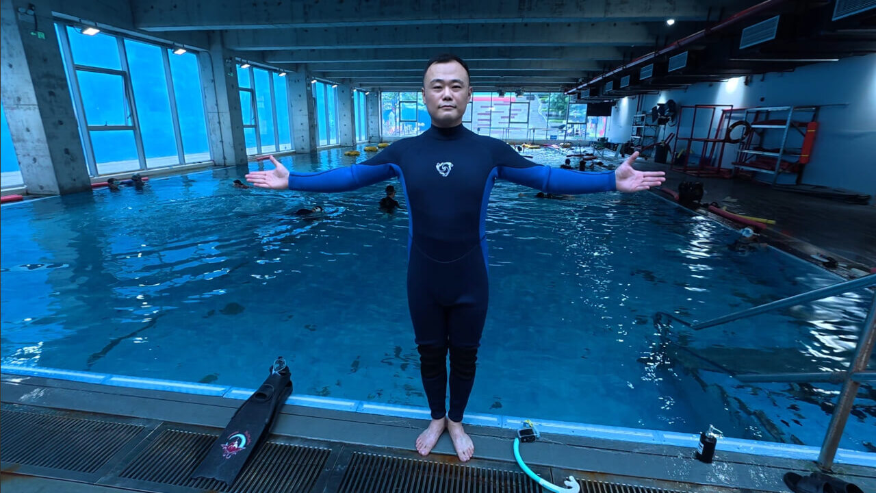 Diver wearing a fitted AquaSwirl full wetsuit with arms extended beside a training pool