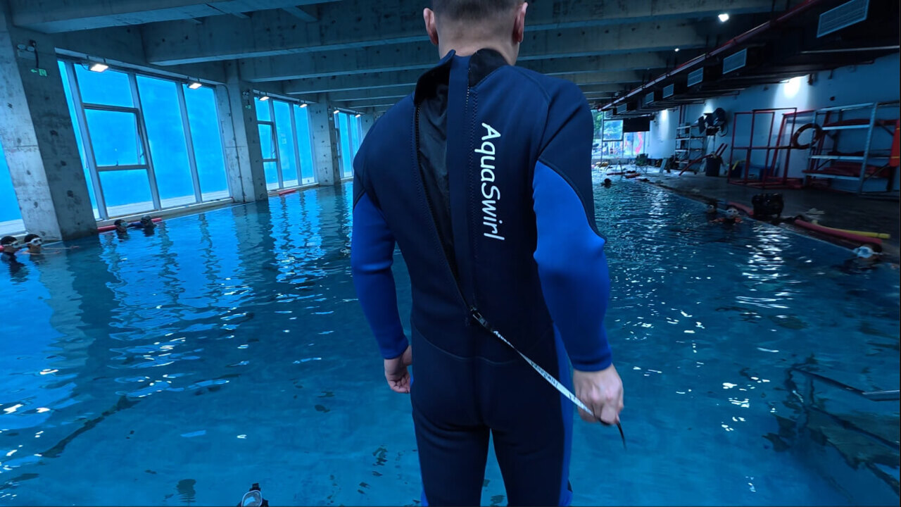 Diver adjusting the back zipper of an AquaSwirl wetsuit beside a training pool